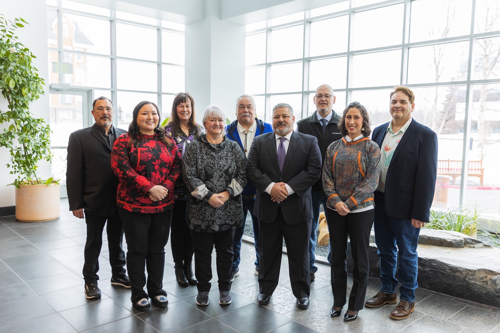 Choggiung Board of Directors and Executive Leadership posing for a photo in a bright lobby with large windows and a potted plant, exhibiting a range of business casual attire and approachable expressions.